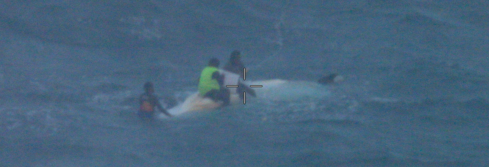 Three people on an overturned boat in the Torres Strait